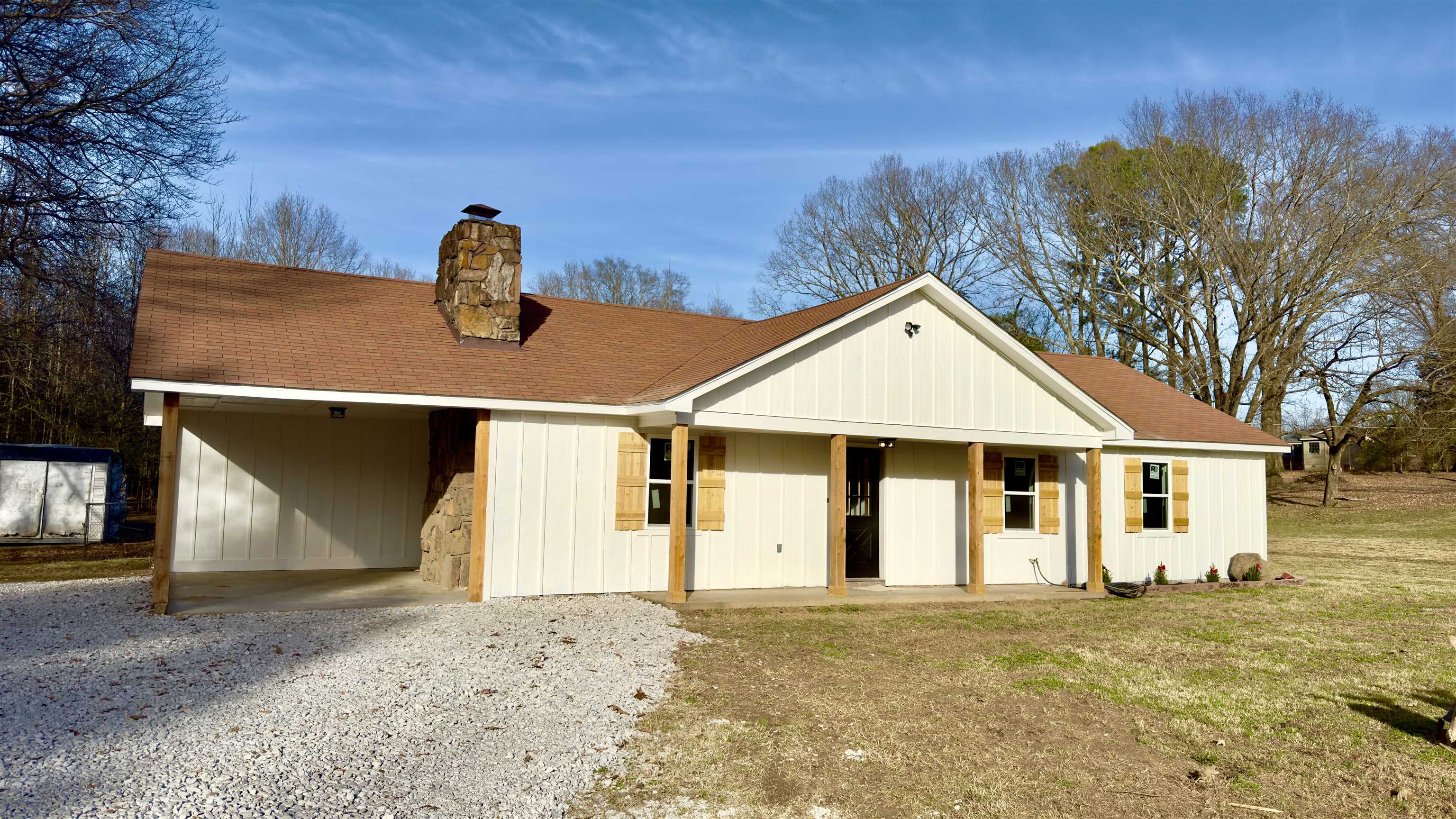 View of front of home featuring a shingled roof, a chimney, gravel driveway, and covered porch