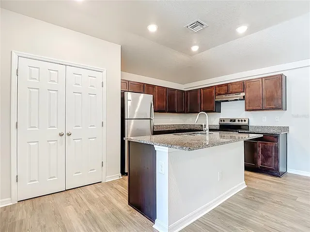 a kitchen with stainless steel appliances granite countertop a refrigerator a sink dishwasher a stove and white cabinets with wooden floor