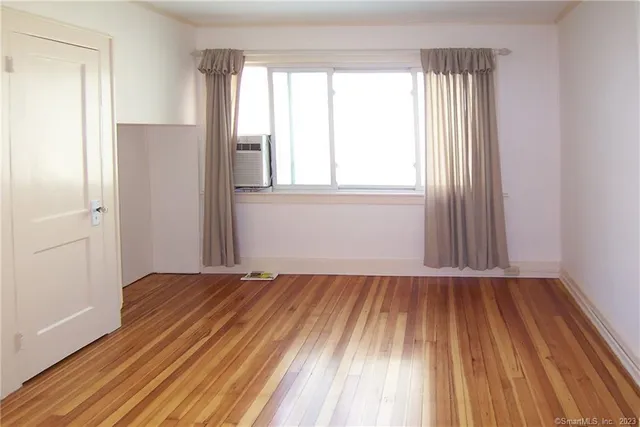 a view of an empty room with wooden floor and a window
