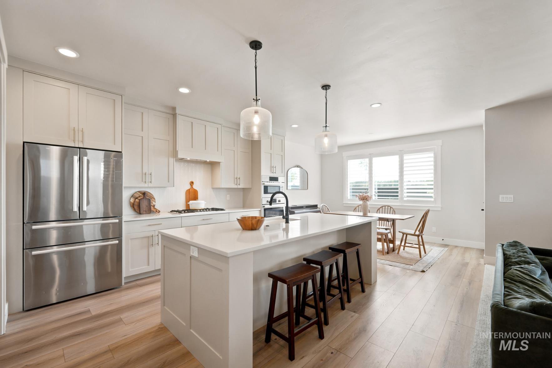 6933 South Zenith Avenue Meridian, ID 83642 - Photo 6 of 34 Modern kitchen featuring a large center island with seating, stainless steel appliances, light-toned cabinetry, and wood-finish flooring