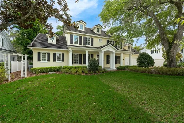 a view of a white house next to a yard with big trees