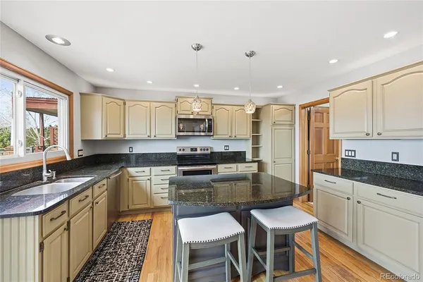 a kitchen with kitchen island granite countertop a sink a stove a refrigerator cabinets and chairs