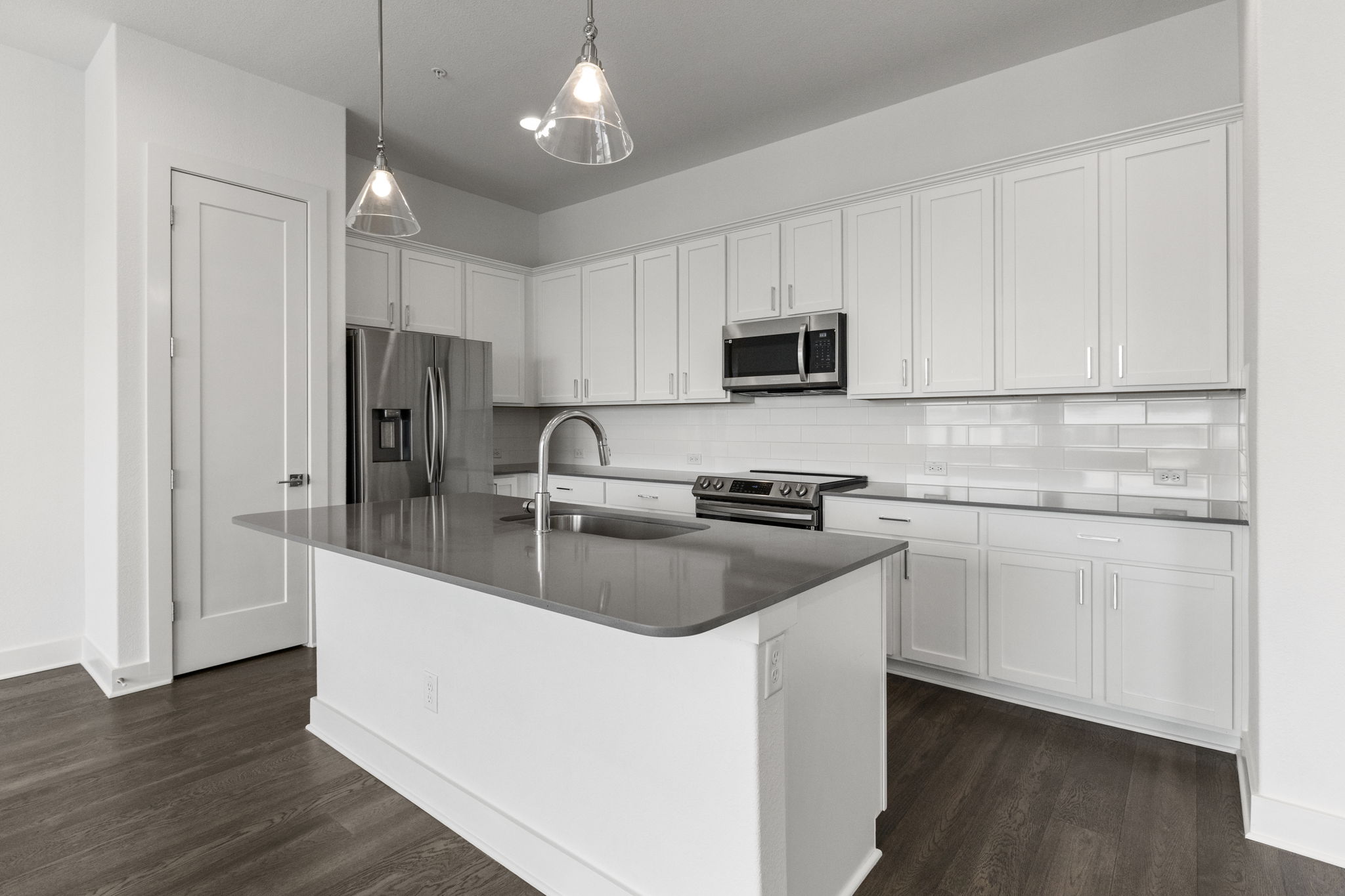 Modern kitchen featuring a central island with an undermount sink, white shaker cabinetry, stainless steel appliances, and wood-finish flooring