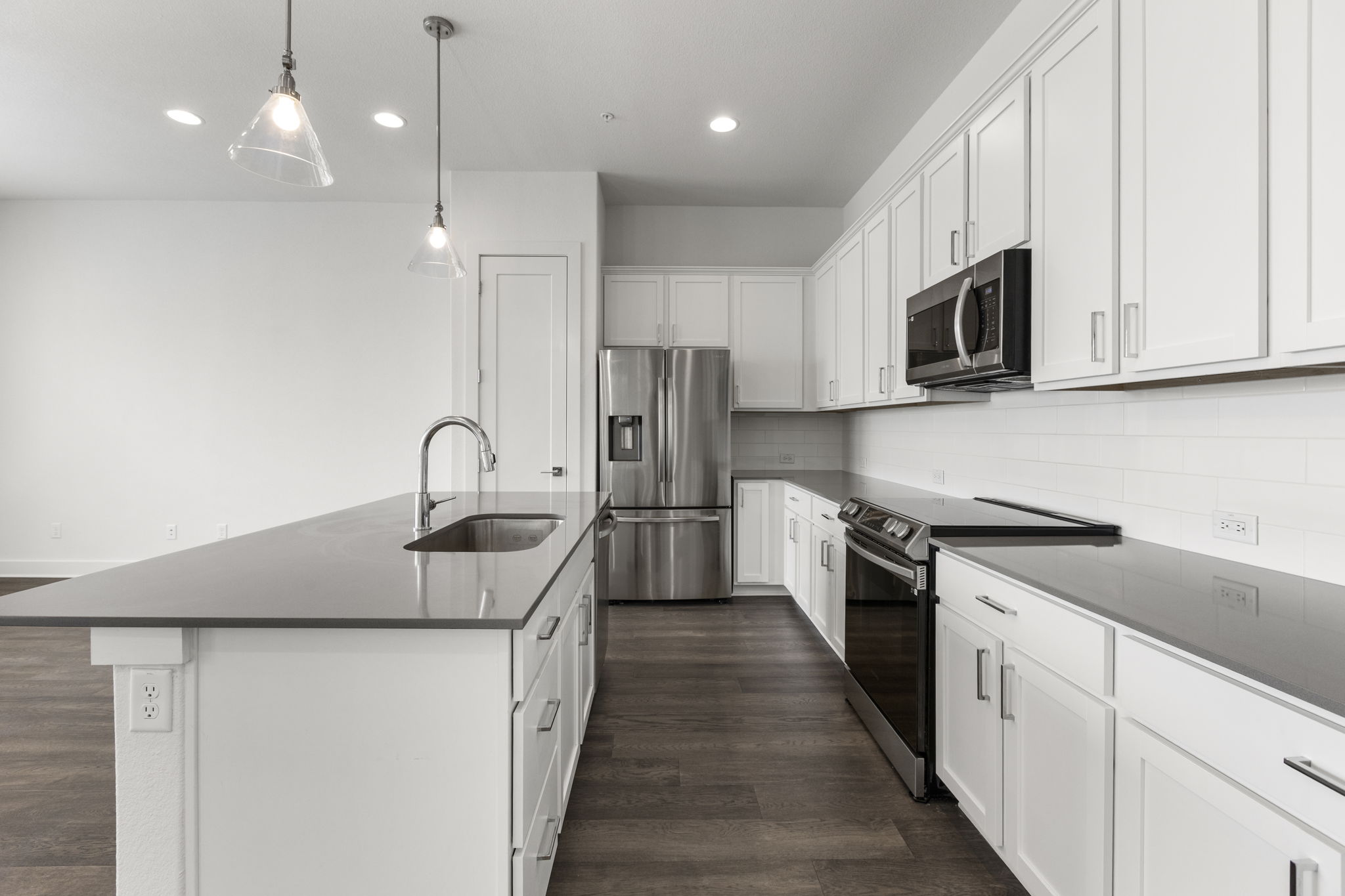 2050 Lohmans Spur Road, Unit 2005 Lakeway, TX 78734 - Photo 2 of 36 Modern kitchen featuring an island with an undermount sink, pendant lighting, white shaker cabinetry, stainless steel appliances, and wood-finish flooring