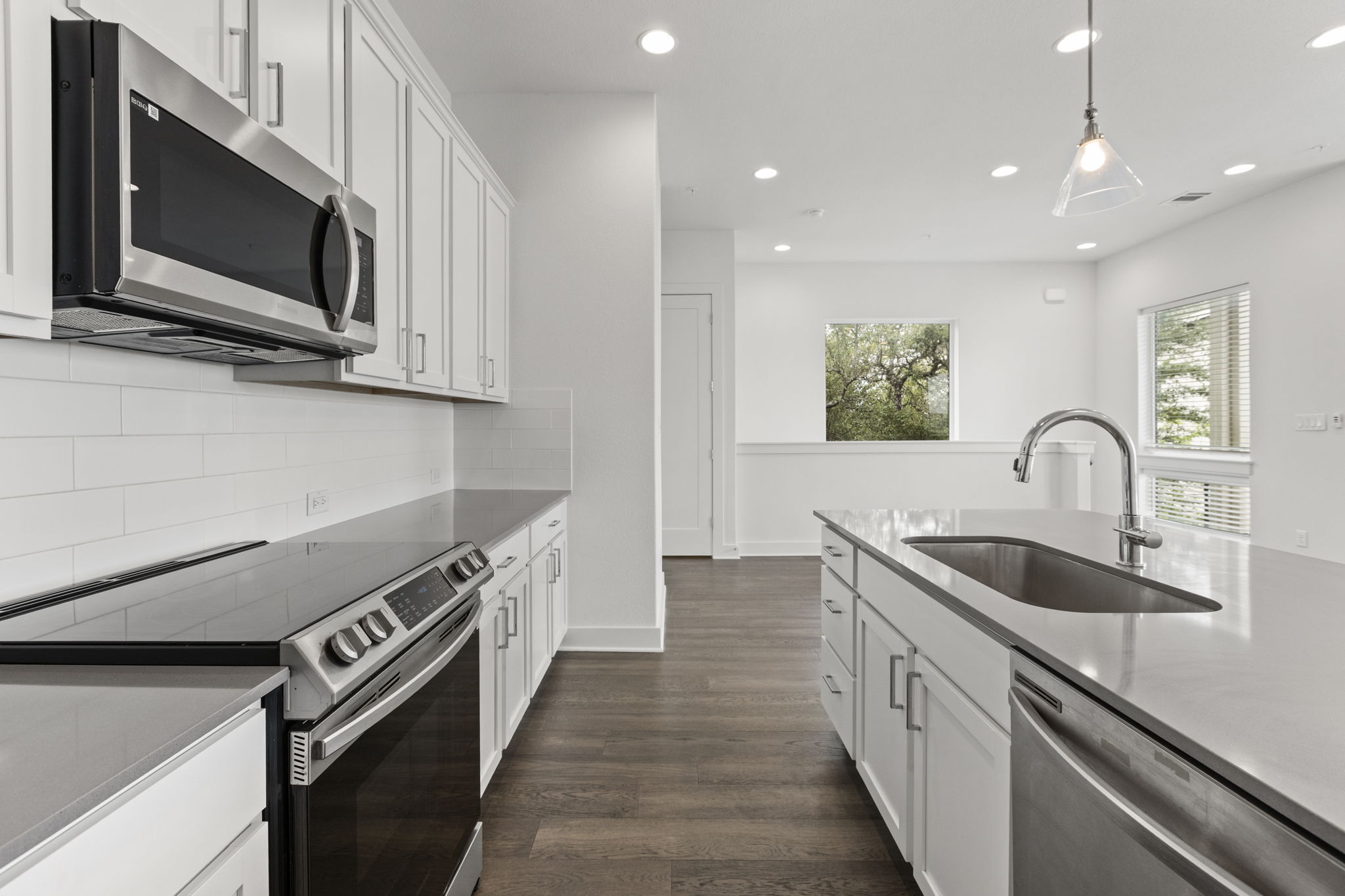 2050 Lohmans Spur Road, Unit 2005 Lakeway, TX 78734 - Photo 3 of 36 Modern kitchen featuring white shaker cabinetry, stainless steel appliances, a subway tile backsplash, light-toned countertops, and wood-finish flooring