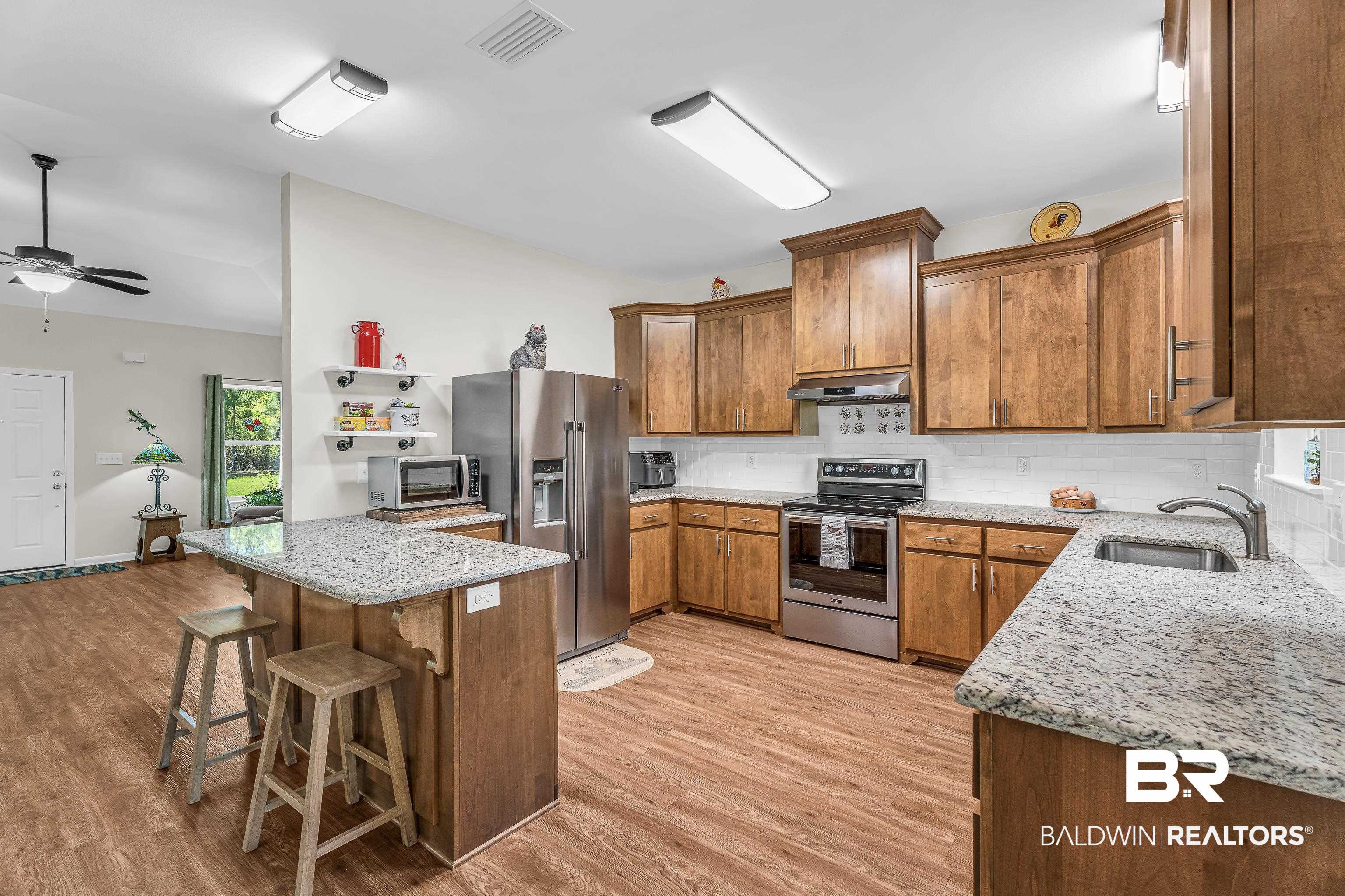 18255 Cactus Court Elberta, AL 36530 - Photo 17 of 53 Kitchen featuring wood finish cabinetry, light stone counters, stainless steel appliances, a kitchen breakfast bar, and vaulted ceiling