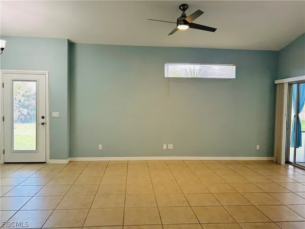 a view of an empty room with window and chandelier fan