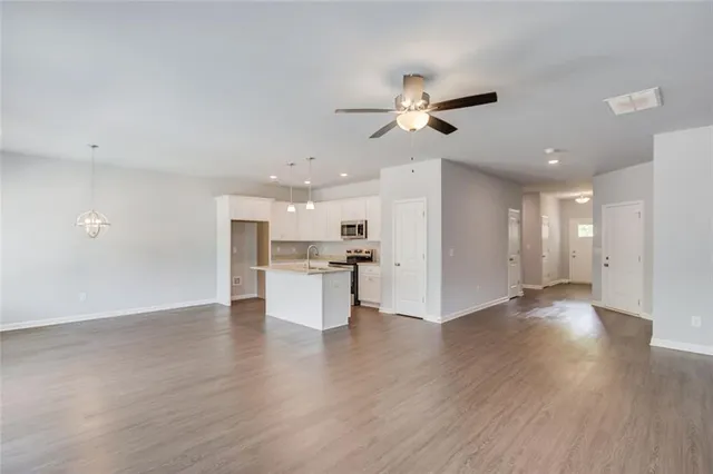 a view of an empty room and kitchen with wooden floor
