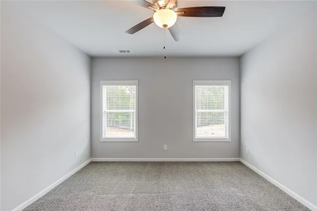 an empty room with chandelier fan and windows