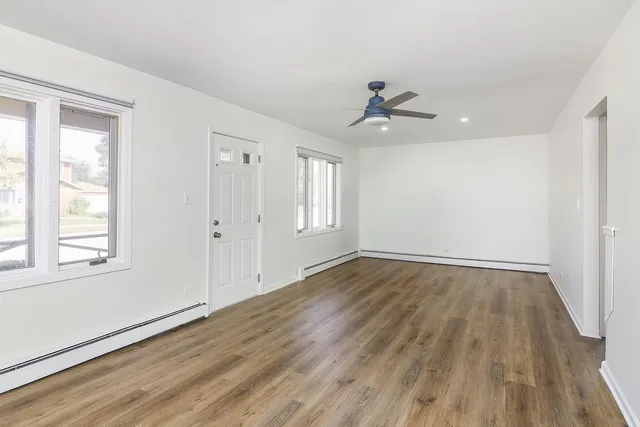 an empty room with wooden floor ceiling fan and windows