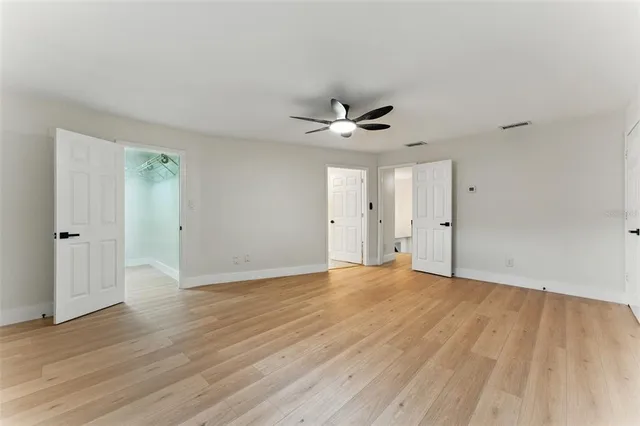 an empty room with wooden floor ceiling fan and windows