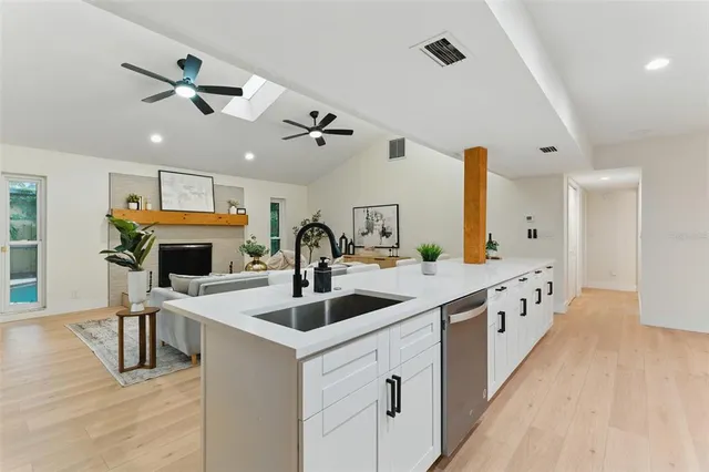 a large white kitchen with stainless steel appliances granite countertop a sink dishwasher and white cabinets with wooden floor