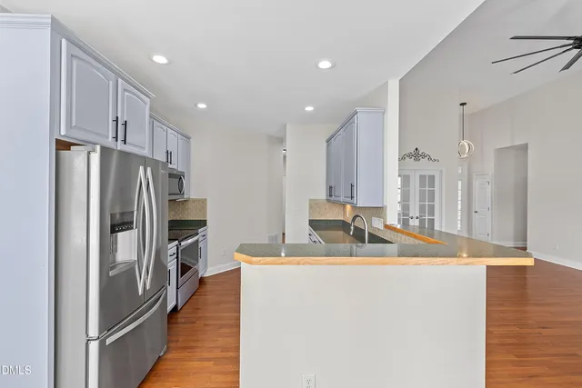 a kitchen with stainless steel appliances granite countertop a refrigerator a sink a stove and a refrigerator with wooden floor