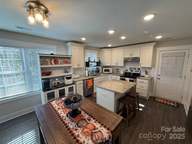 a kitchen with stainless steel appliances granite countertop a refrigerator a sink dishwasher a stove and a dining table with wooden floor