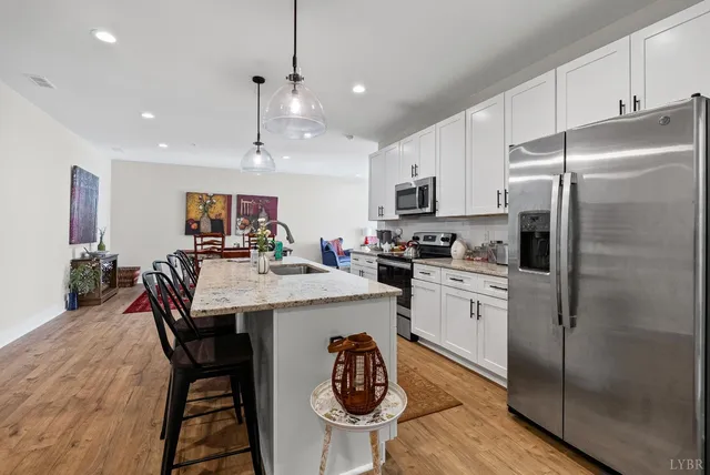 a kitchen with stainless steel appliances granite countertop a refrigerator a stove a sink a dining table and chairs with wooden floor