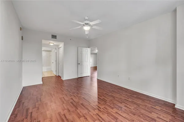 a view of an empty room with wooden floor and a ceiling fan
