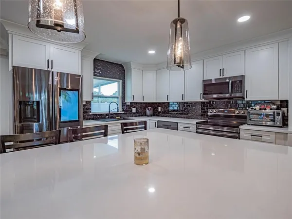 a large kitchen with stainless steel appliances a large counter top cabinets and a chandelier