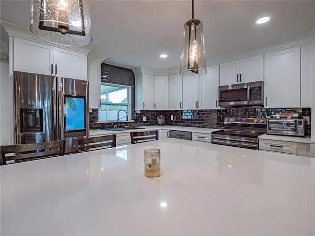 a large kitchen with stainless steel appliances a large counter top cabinets and a chandelier