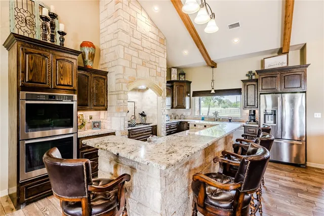 a kitchen with stainless steel appliances kitchen island granite countertop a stove a refrigerator a sink dishwasher a dining table and chairs with wooden floor