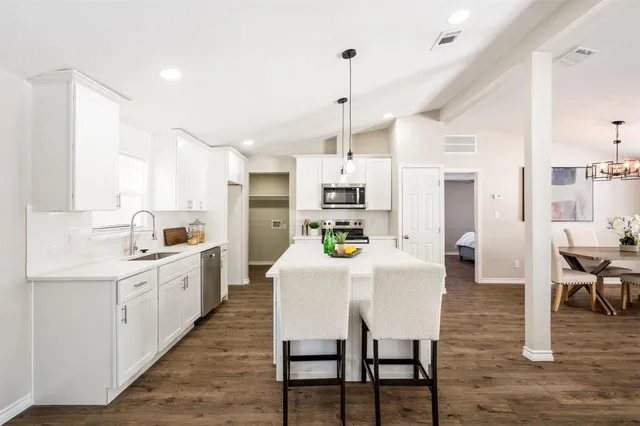 a large white kitchen with stainless steel appliances kitchen island granite countertop a table chairs and a refrigerator