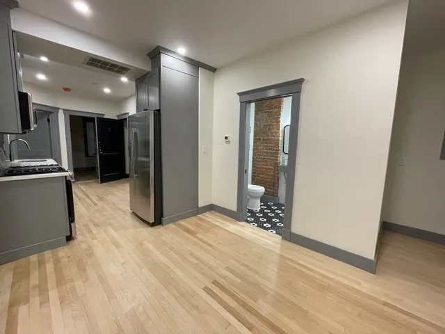 a view of an empty room with wooden floor and a kitchen