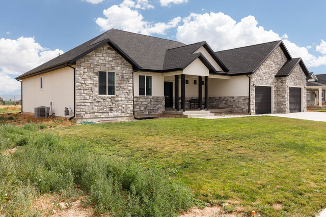 186 West 580 North Redmond, UT 84652 - Photo 49 of 74 View of front of property with stone siding, a front lawn, a porch, and an attached garage