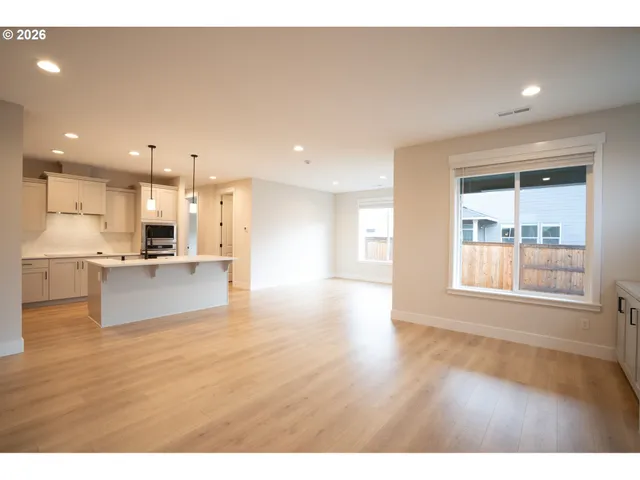 a view of an empty room with kitchen and window