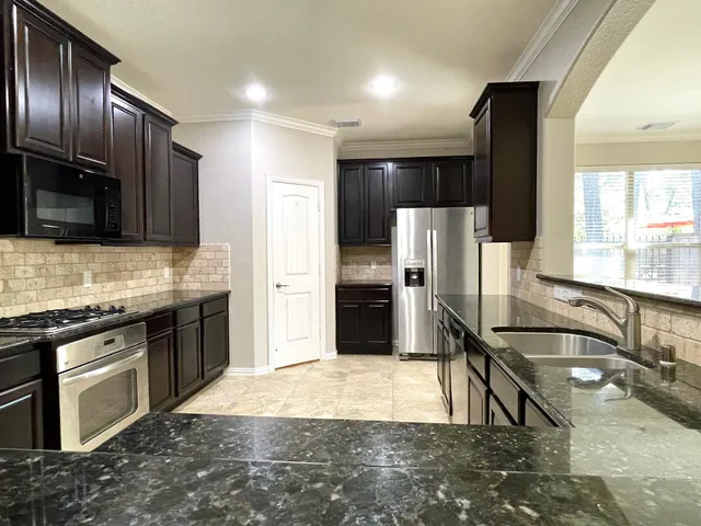 a kitchen with stainless steel appliances granite countertop a refrigerator a stove and a sink with wooden cabinets