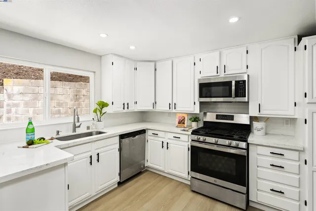 a white kitchen with stainless steel appliances a sink a stove and cabinets