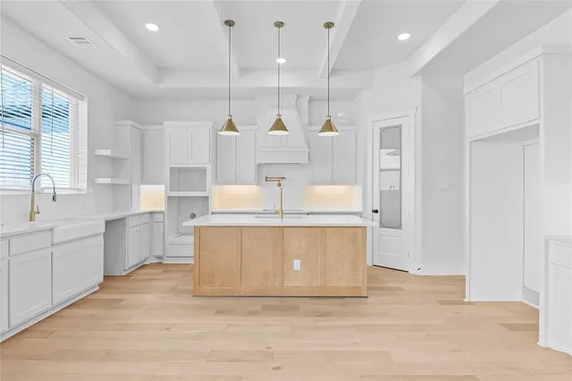 a large kitchen with stainless steel appliances kitchen island granite countertop a stove a sink a refrigerator and white cabinets with wooden floor