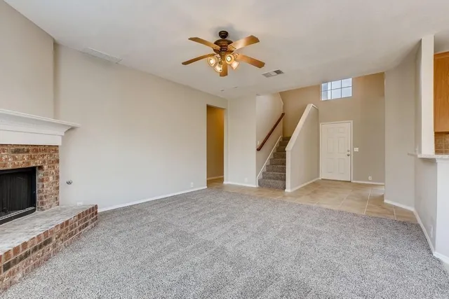 a view of an empty room with chandelier fan and fire place