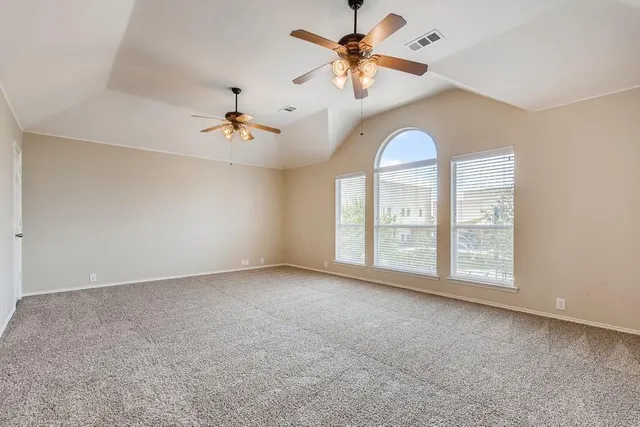 an empty room with chandelier fan and windows