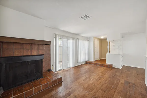 a view of an empty room with wooden floor fireplace and a window