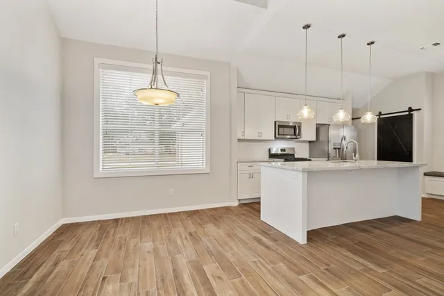 a kitchen with stainless steel appliances granite countertop a refrigerator a stove and white cabinets with wooden floor