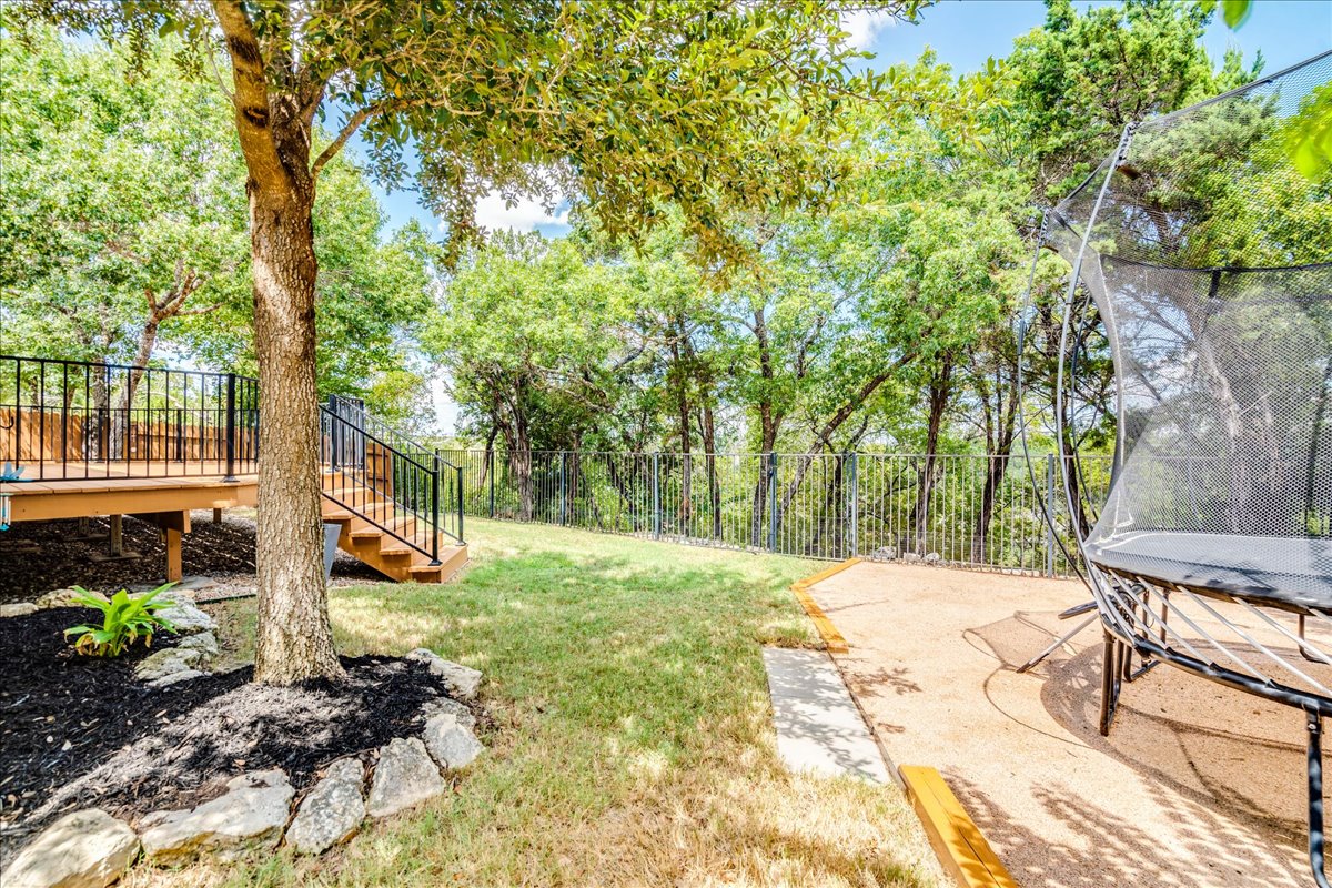 5009 Inks Clearing Lane Austin, TX 78738 - Photo 8 of 34 Mature trees frame a grassy lawn bordered by a wrought iron fencing and a wooden deck.