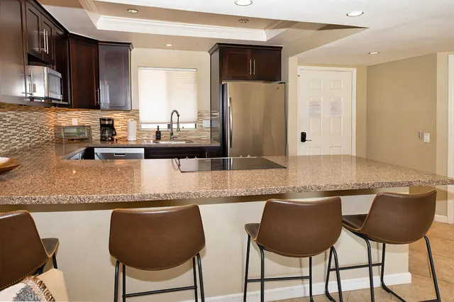 a kitchen with granite countertop a counter space chairs cabinets and stainless steel appliances