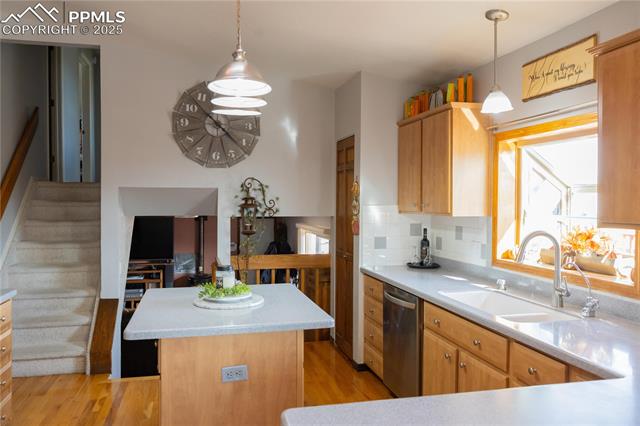 8115 Mustang Road Colorado Springs, CO 80908 - Photo 13 of 48 Kitchen featuring light wood-type flooring, a kitchen island, stainless steel dishwasher, decorative backsplash, and hanging light fixtures