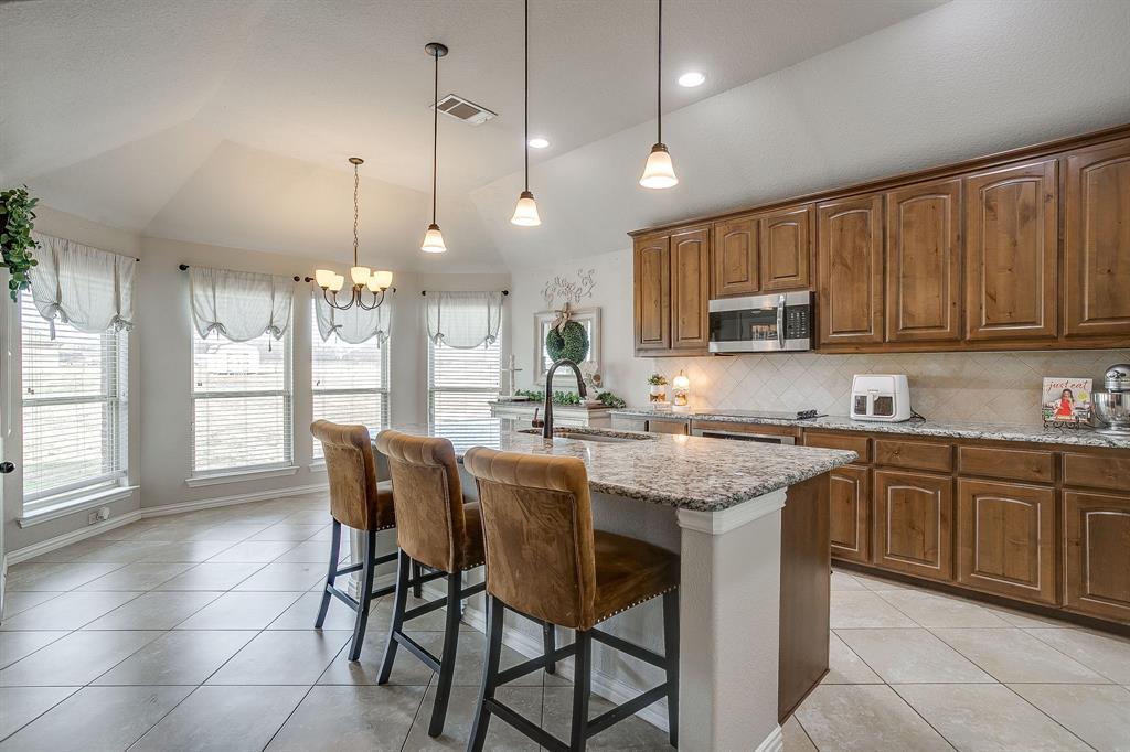 8005 Canyon Ridge Drive Godley, TX 76044 - Photo 11 of 40 a kitchen with stainless steel appliances granite countertop wooden cabinets a stove a sink a dining table and chairs