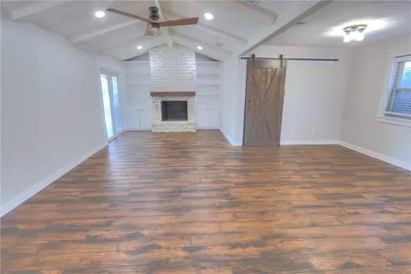 an empty room with wooden floor a ceiling fan a fireplace and entryway