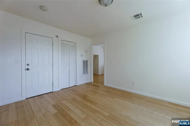 a view of an empty room with wooden floor and closet