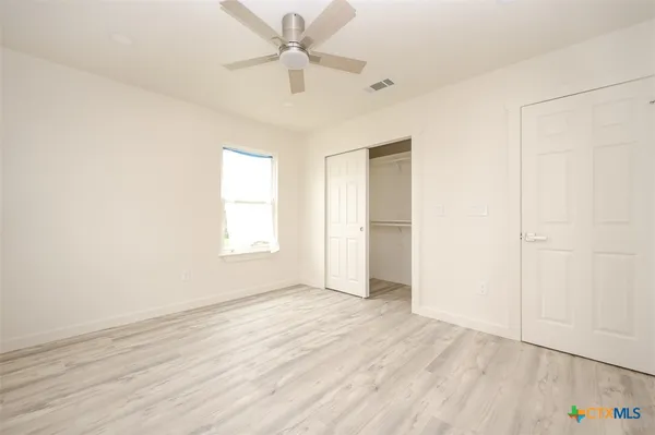 an empty room with wooden floor fan and windows