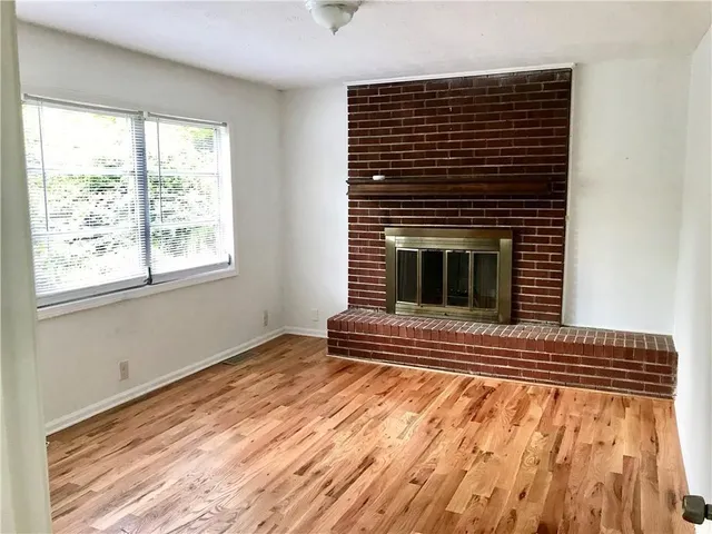 a view of an empty room with wooden floor fireplace and a window