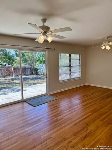 an empty room with wooden floor fan and windows