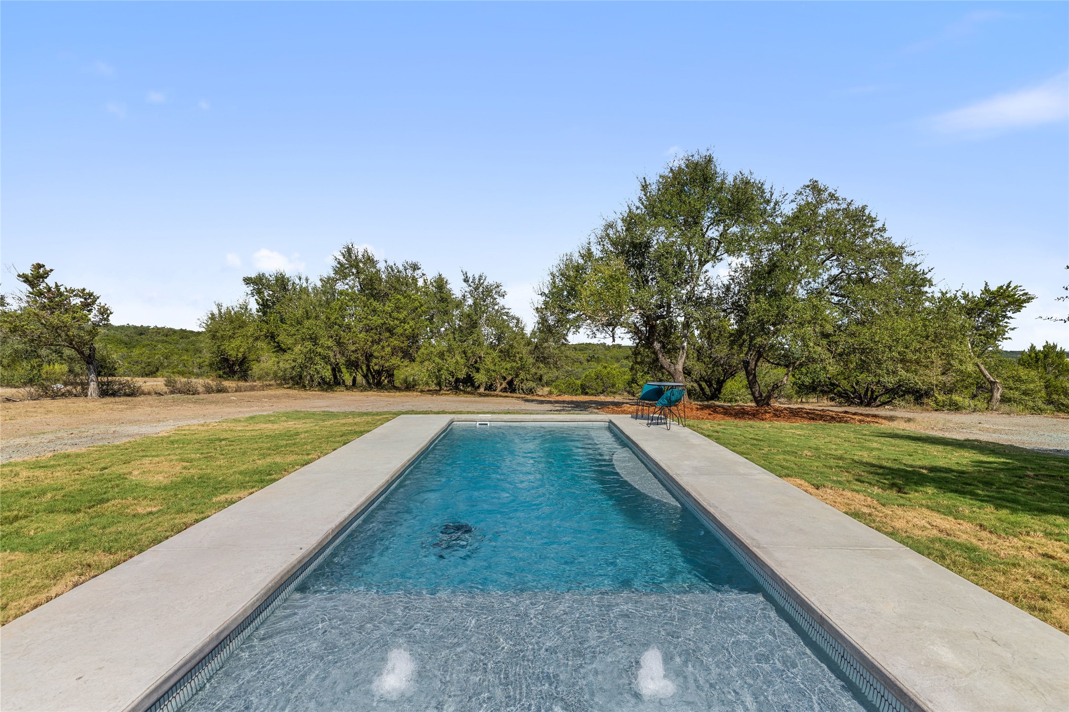 601 Hays Country Acres Road Dripping Springs, TX 78620 - Photo 36 of 38 A sparkling swimming pool surrounded by a concrete deck overlooks scenic tree-lined views.