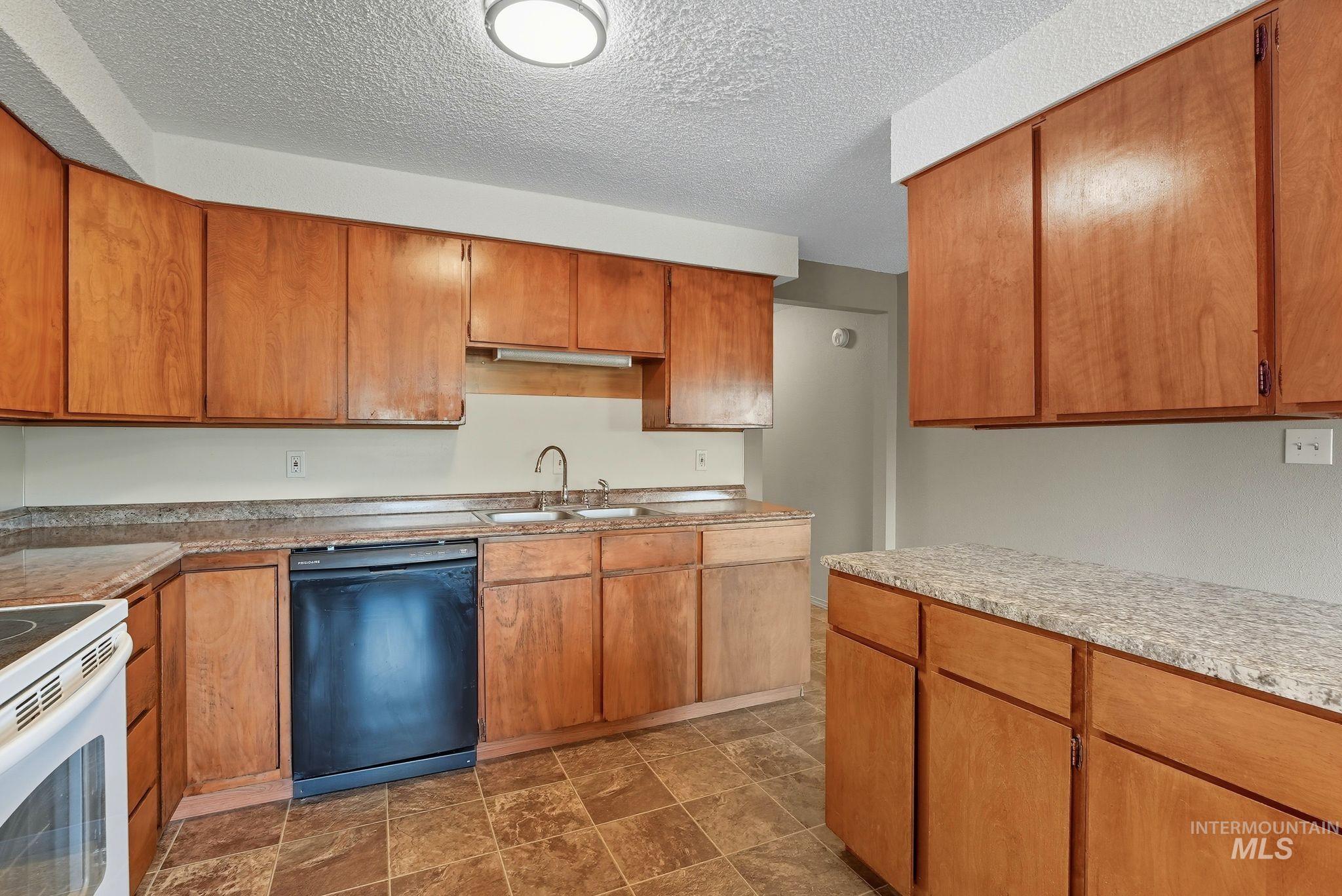 1101 5th Street Asotin, WA 99402 - Photo 35 of 48 Kitchen with black dishwasher, brown cabinets, a textured ceiling, and white electric range