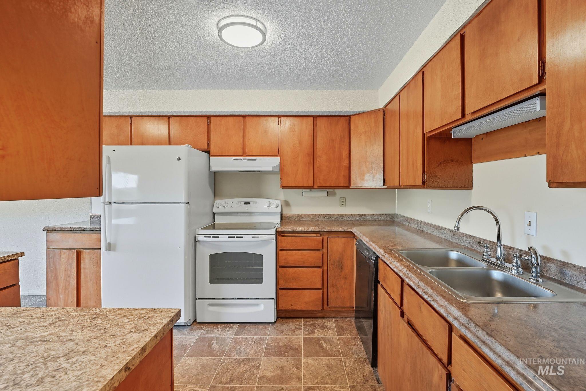 1101 5th Street Asotin, WA 99402 - Photo 35 of 48 Kitchen featuring white appliances, brown cabinets, a textured ceiling, under cabinet range hood, and stone finish floors