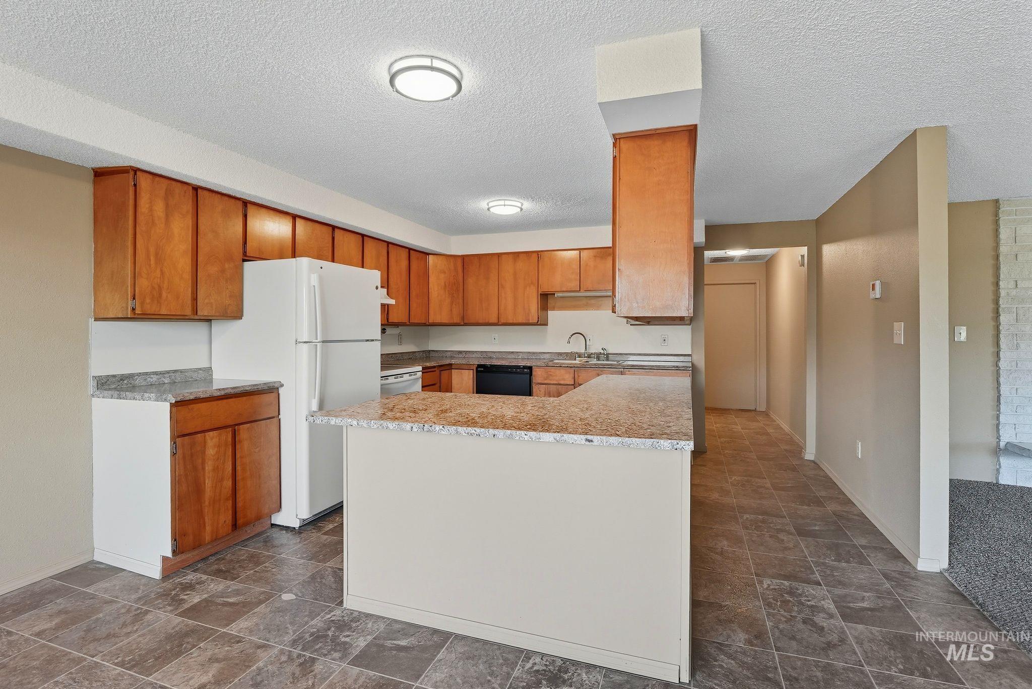 1101 5th Street Asotin, WA 99402 - Photo 37 of 48 Kitchen with freestanding refrigerator, light countertops, brown cabinetry, a textured ceiling, and dishwasher
