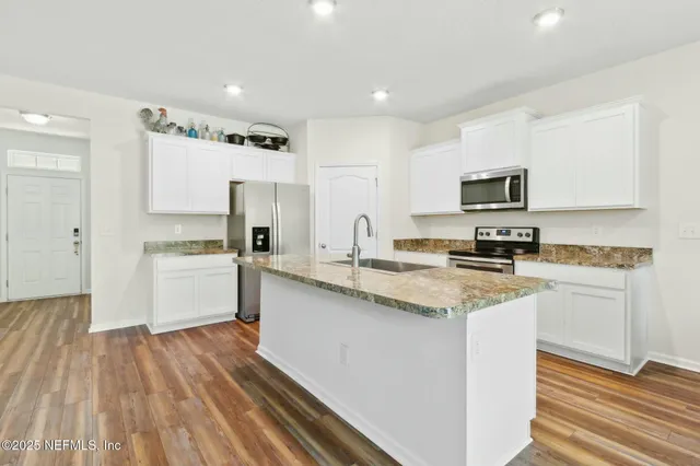 a kitchen with stainless steel appliances a sink dishwasher a refrigerator and white cabinets with wooden floor