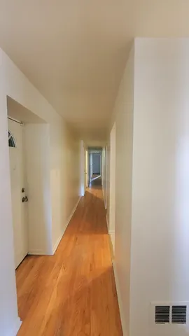 a view of a hallway with wooden floor and a bathroom