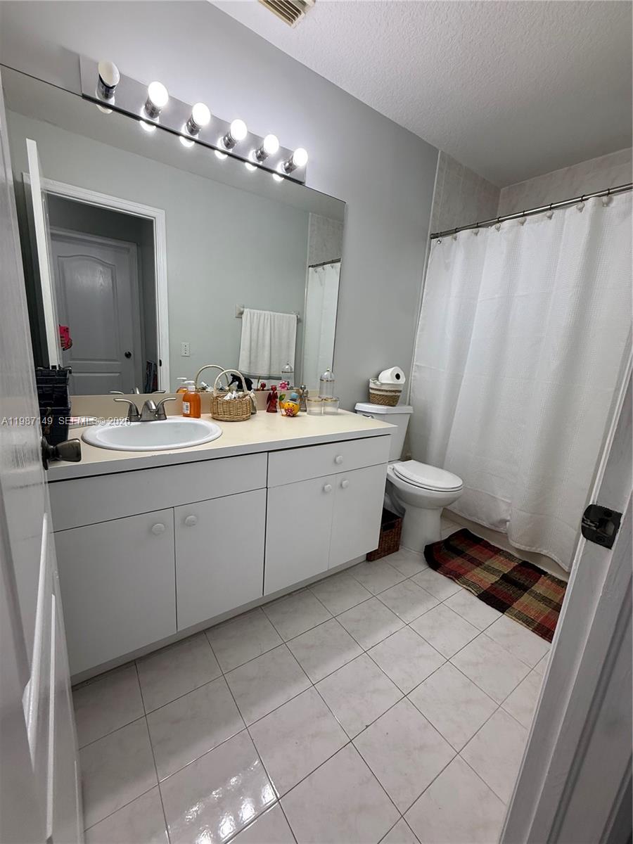 18164 Southwest 149th Place Miami, FL 33187 - Photo 26 of 30 a bathroom with a double vanity sink a toilet a mirror and shower curtain
